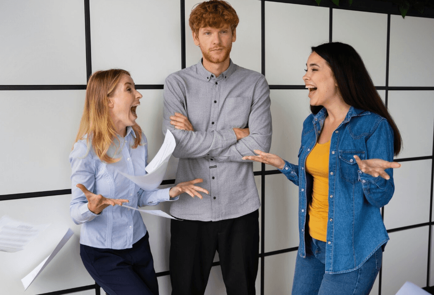 Employees engaged in a heated workplace discussion while a colleague stands between them, illustrating conflict resolution and difficult conversations in the workplace.